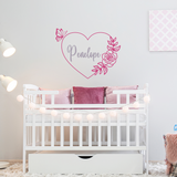 White crib with pink pillows in a nursery with a decorative wall decal.