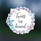 Sticker with 'Twins on board' text surrounded by butterflies and leaves on a dark background.